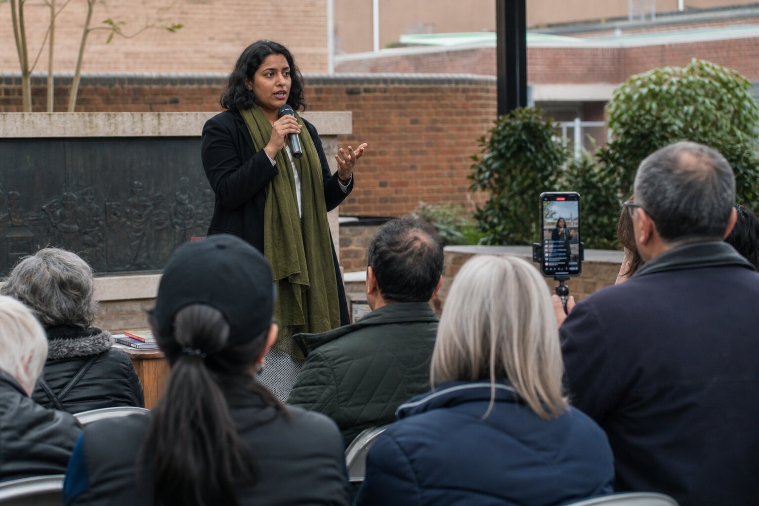 Community speaker addressing an audience while a phone streams the event.