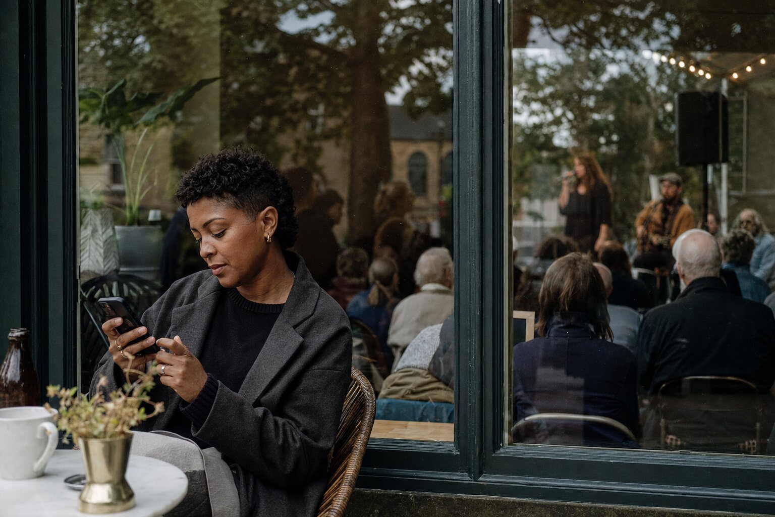 Person using a phone beside a public community event reflected in glass.